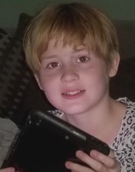 Photo of Chloe Hobbs, a girl with fair skin and strawberry-blonde hair in a boy cut. She is holding a tablet PC and gazing at the camera withe a slight smile on her face.