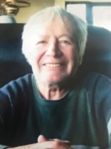 Photo of a white-haired, fair-skinned elderly man wearing a soft gray sweater and smiling for the camera.