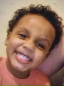 Photo of a small African-American boy, grinning with his teeth clenched. The photo is taken at an angle.