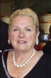 Photo of a blonde woman wearing pearl necklace and earrings; her hair is cut short and she is smiling for the camera.