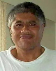 Photo of Bruce Rangitutia, a middle-aged man smiling awkwardly at the camera. He is wearing a white T-shirt; his skin is tan, and his hair is salt-and-pepper, cut short.