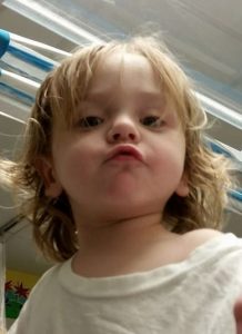 Photo of a toddler boy with a halo of blond hair, pursing his lips at the camera.