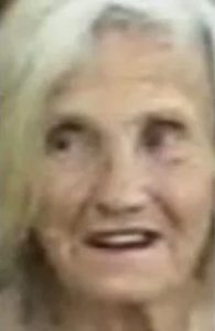 Blurry photo of a white-haired old lady with pale, wrinkled skin, her mouth open as though she is about to speak.