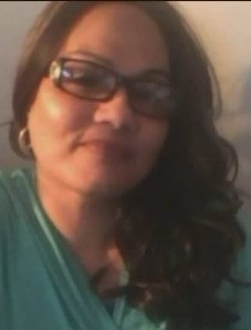 Photo of a middle-aged woman with long curly dark hair and light-brown skin, wearing horn-rimmed glasses and a teal sweater.