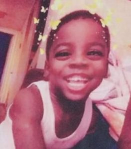 Photo of Jakie Toole, a smiling child in a white tank top. He has short dark brown hair and brown skin. A filter has been applied that adds yellow butterflies around his head.