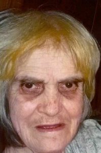 Photo of an older woman with straight white hair dyed partly blonde and dark circles under her eyes.