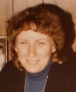 Photo of a middle aged woman with curly chin-length auburn hair and pale skin, smiling for the camera.