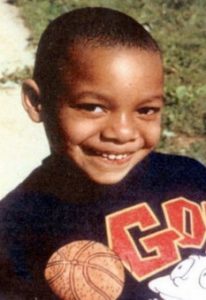 Photo of a small boy with a buzz cut, wearing a basketball sweatshirt.