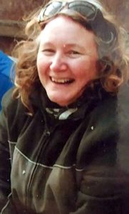 Photo of Ann Pomphret, a large woman with curly hair, dressed for the outdoors, grinning at the camera.