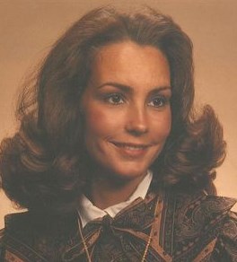 Sepia-tone photo of a woman with an old-fashioned hairstyle, cut shoulder-length and curled up at the ends, wearing professional attire.