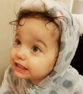 Photo: A toddler girl with wet hair, wrapped in a terrycloth robe with hood. She has brown eyes and light-tan skin.