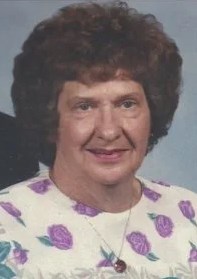 Photo of an older woman with short, permed brown hair, wearing a flower-print dress.