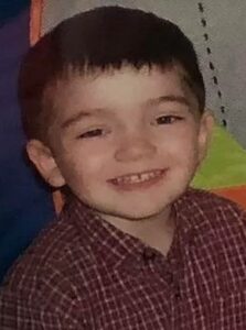 Photo of a small boy in a red-checked collared shirt. He has straight brown hair and light skin.