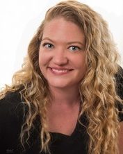 Portrait photo of a young woman with fair skin and long curly blond hair, smiling for the camera.