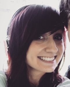 Photo of a young woman with dark hair and pale skin, smiling for the camera.