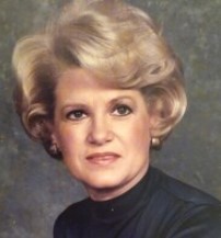Portrait photo of a woman with short, permed blonde hair, fair skin, and brown eyes.