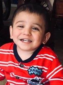 Photo of a small, smiling boy wearing a red striped shirt. He has light skin and short brown hair.