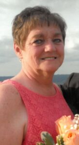 Photo of a middle-aged woman with short brown hair and fair skin, wearing a peach tank top and holding flowers.