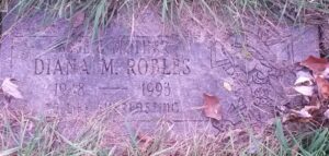 Photo of an overgrown gravestone. It reads, "Wife and mother Diana M. Robles. 1948-1993. To life everlasting."