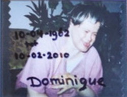 Blurry photo of a woman with Down syndrome. She is wearing a pink shirt, and her eyes are scrunched up in laughter, her tongue poking slightly from her mouth. She has pale skin and short brown hair with blonde streaks.