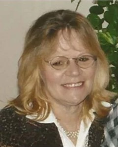 Photo of middle-aged woman with curly blonde hair, pale skin, and glasses, smiling for the camera.