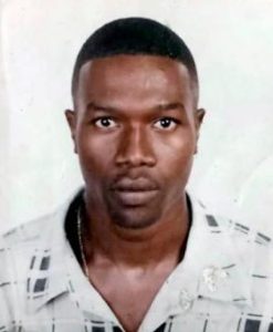 Photo of a black man with short hair, wearing a white button-up shirt.