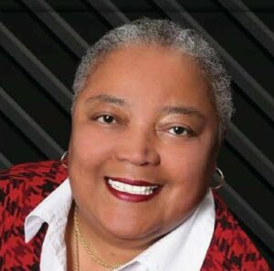 Portraint photo of an older woman with dark skin and short gray hair, wearing make-up, earrings, and a red top with a white collar.