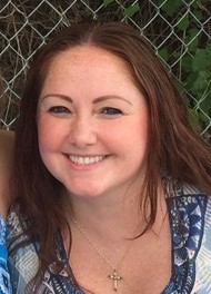 Photo of a woman with fair skin, a round face, long brown hair, and a wide smile. She is wearing light, neatly done make-up.