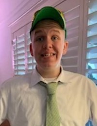 Photo of a teenage boy with pale skin, wearing a green baseball cap and white dress shirt with a light-green tie. He is smiling awkwardly.