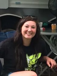 Photo of a young woman wearing a black T-shirt. Her hair is long and dark, and her skin is fair; she has a pair of sunglasses propped on her head.