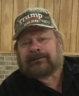 Photo of a bearded older man wearing a Trump 2020 baseball cap.