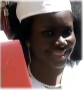 Photo of a young woman with dark-brown skin, smiling, in a white graduation cap.