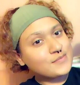 Photo of a young adult with curly brown hair, tan skin, and dark-brown eyes, wearing a green headwrap and a nose ring.