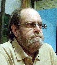 Photo of a balding middle-aged man with glasses, a collared shirt, and a serious expression.