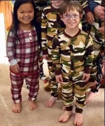 Photo: A teenage girl and a boy, both with short limbs. The girl is wearing red-and-white checked pajamas; she has olive skin and straight black hair. The boy is wearing camouflage pajamas and glasses; he has fair skin, blond hair, and glasses. They are smiling for the camera.