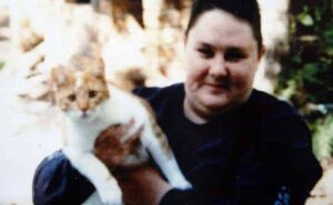 Photo: A blurry image of a young woman with very short brown hair and pale skin, wearing a black sweater. She is holding an orange-and-white cat. 