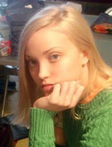 Profile photo of a young blond woman sitting with her head propped on her hand. She is wearing a green sweater.