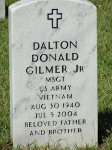 Photo: A white marble gravestone decorated with a cross, reading "Dalton, Donald Gilmer Jr., Msgt US Army, Vietnam, August 30 1940 to July 5 2004, beloved father and brother."