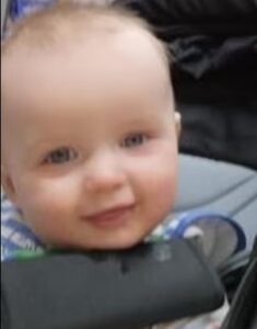 Blurry photo of a fair-skinned baby with blue eyes and scant, dark-blond hair.