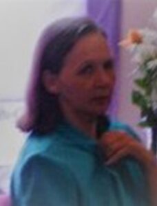 Photo of a middle-aged woman with shoulder-length brown hair and light skin, wearing a teal blouse.