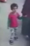 Blurry image of a child wearing a red shirt; she has short dark hair and tan skin; she is holding hands with an adult off to the right of the frame.