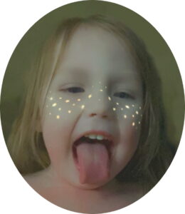 Photo: Toddler girl with wispy blond hair and pale skin, sticking out her tongue at the camera. A filter has been applied, giving her sparkly freckles across the brdige of her nose and cheeks.
