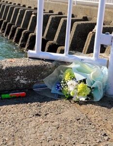 Concrete bridge and white railing above water. A bunch of yellow flowers has been left at the curb.