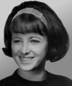 Black and white photo of a smiling, light-skinned woman with her dark hair in a bob, held back by a hair band.