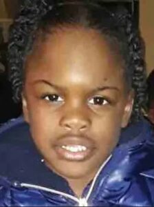 Photo of a young girl with brown skin and black hair in tight braids. She is wearing a puffy blue jacket.