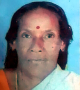 Photo of an older Indian woman with long black hair and light brown skin; she has a red bindi on her forehead and is wearing white and orange clothing.