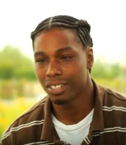 Photo of an African American man with medium-brown skin, his hair in neat braids, wearing a brown polo shirt.