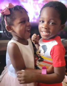 Two young African-american children, a girl wearing a pink dress and hair ribbon, and a boy wearing a red Mickey Mouse shirt.