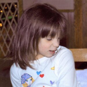 Photo of a girl with pale skin and straight brown hair, wearing a white shirt, looking down and to the right.