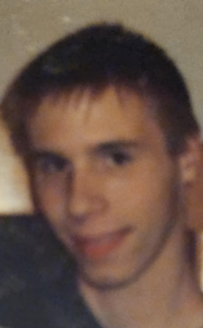 Blurry photo of a young man with dark hair, brown eyes, and light skin, smiling for the camera.